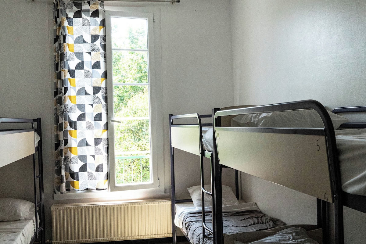 Ein Schlafsaalzimmer mit Etagenbetten, Deckenventilator, Fenster mit geometrischem Vorhang und Heizkörper.