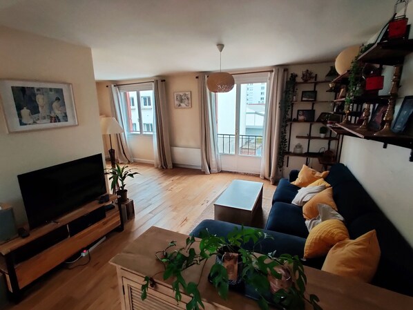 Un salon avec un téléviseur, un canapé, une table basse et des plantes.
