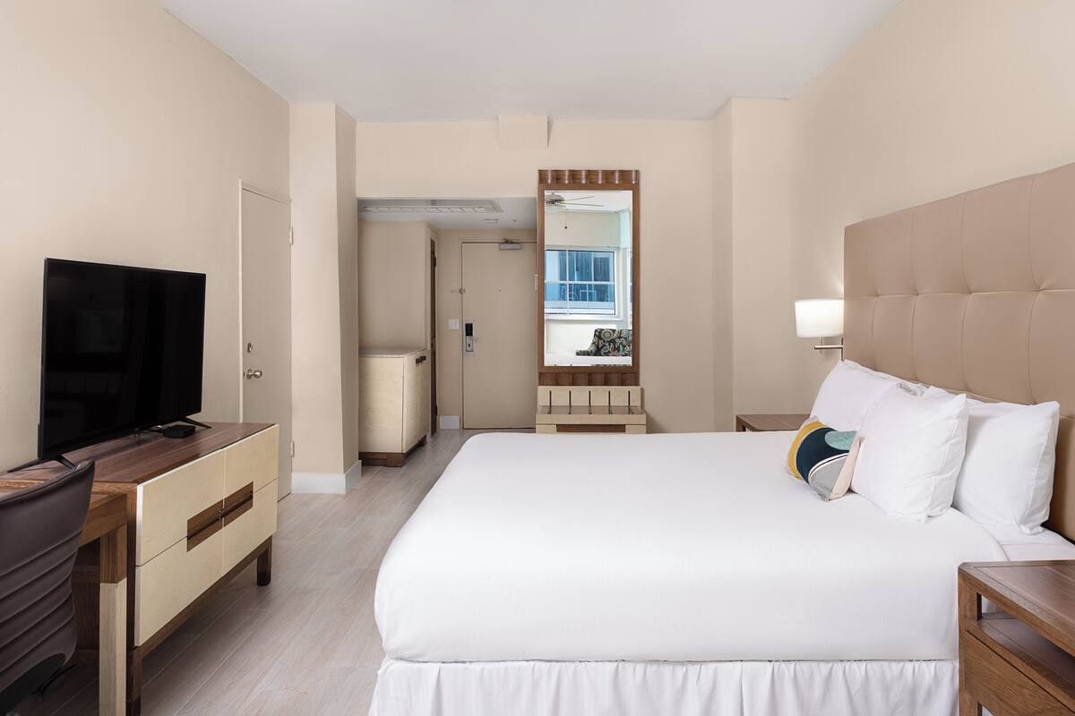 A hotel room with a bed, a TV, a desk, and a mirror.