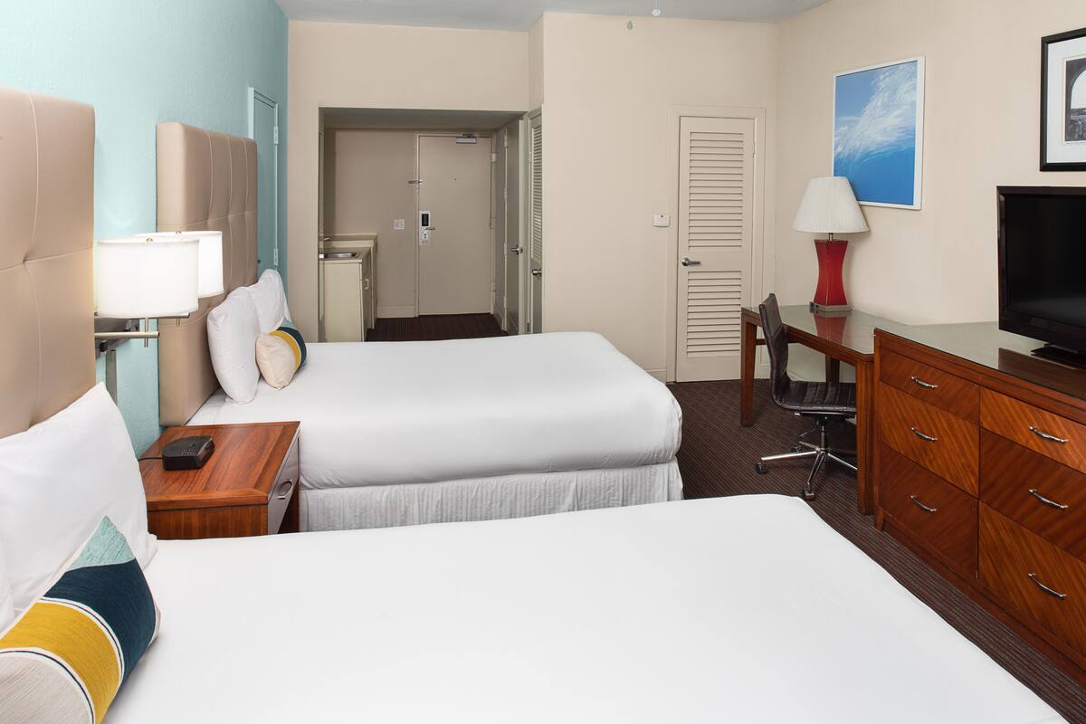 A hotel room with two beds, a desk, a TV, and a bathroom door.
