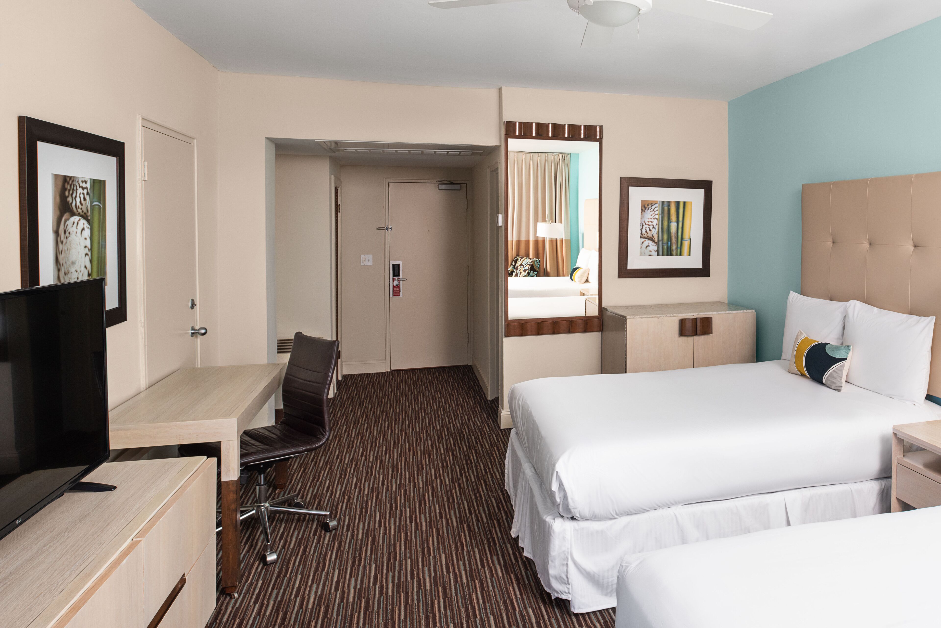 A hotel room with a bed, a desk, a chair, a TV, and a door.