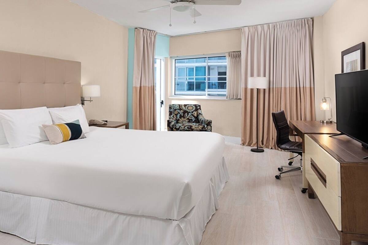 A hotel room with a large bed, a desk with a chair, a TV, and a window with curtains.