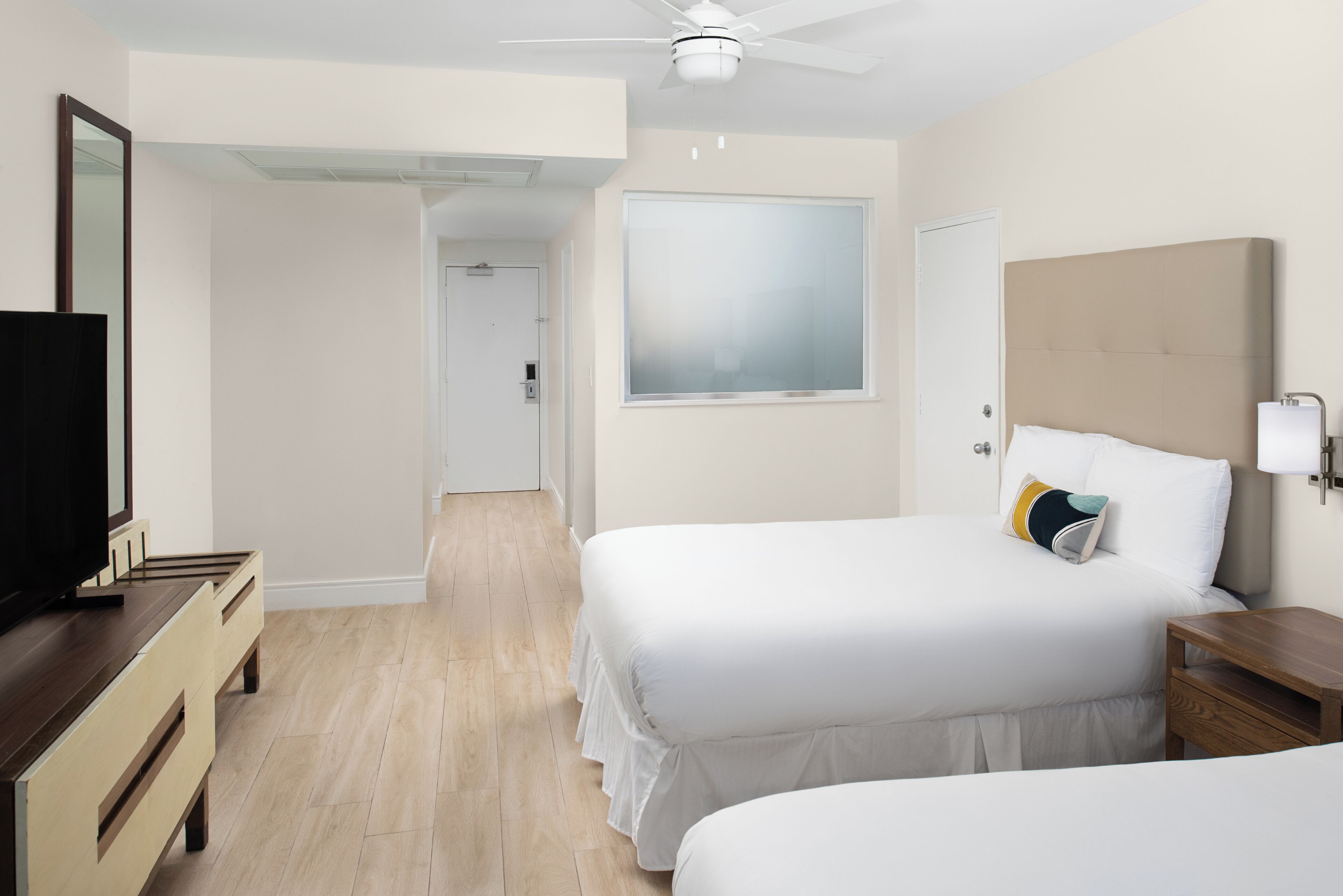 A hotel room with two beds, a TV, a dresser, and a large window.