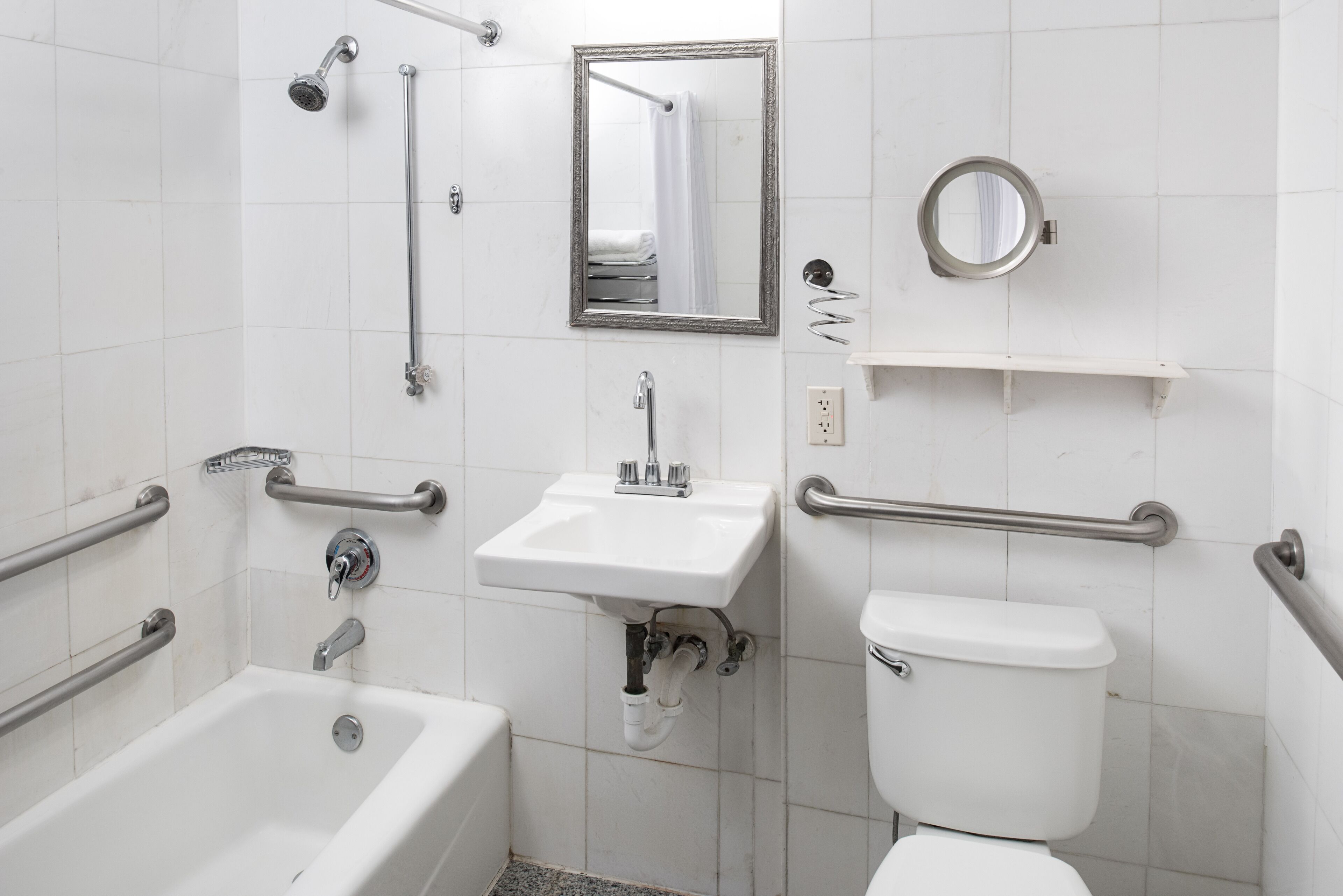 A bathroom with a bathtub, sink, toilet, and grab bars.
