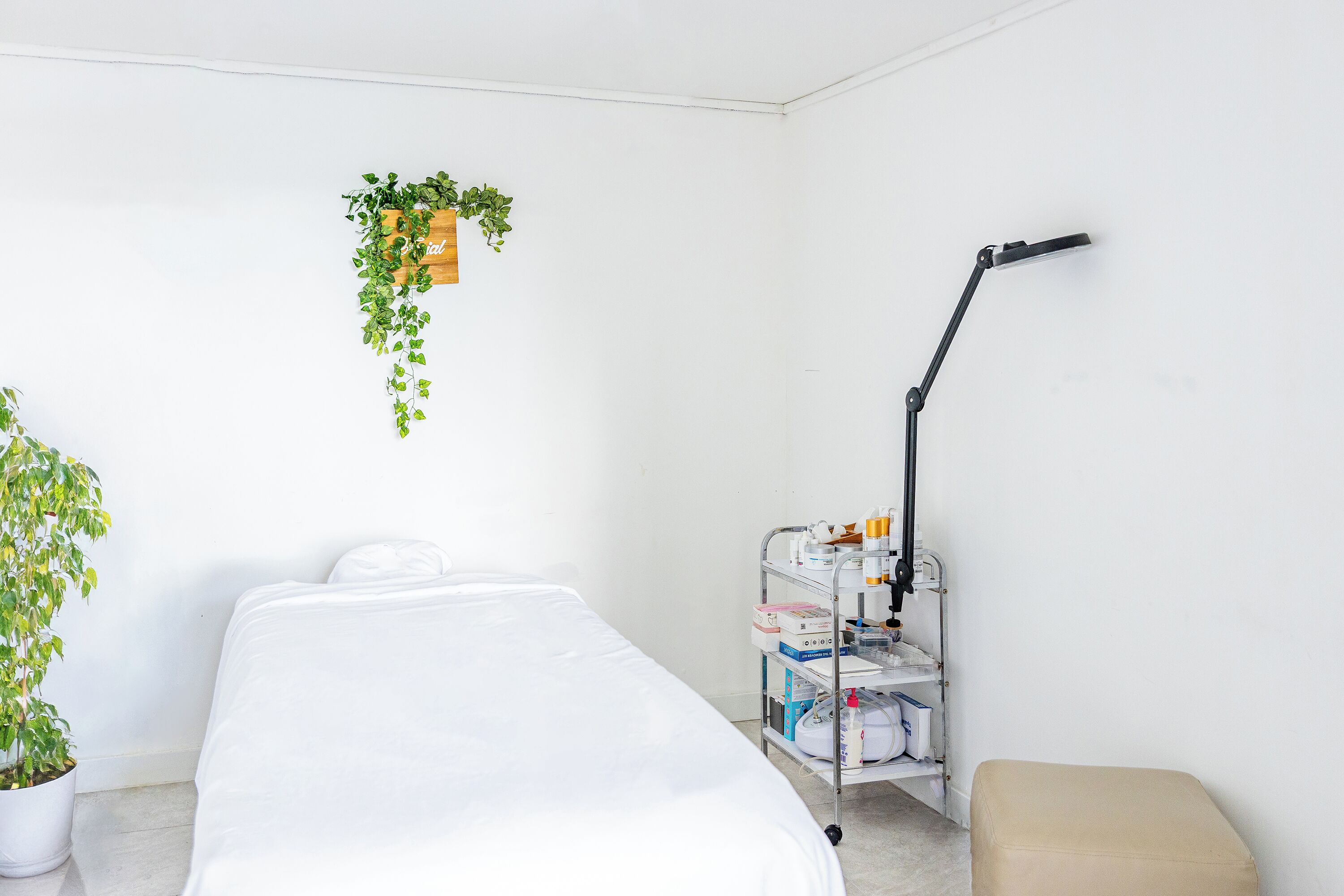 A clean, white room with a bed, a small table with a lamp, and a shelf with medical supplies.