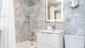 Un bagno moderno con parete doccia in marmo, ripiano in vetro, lavandino bianco e water.