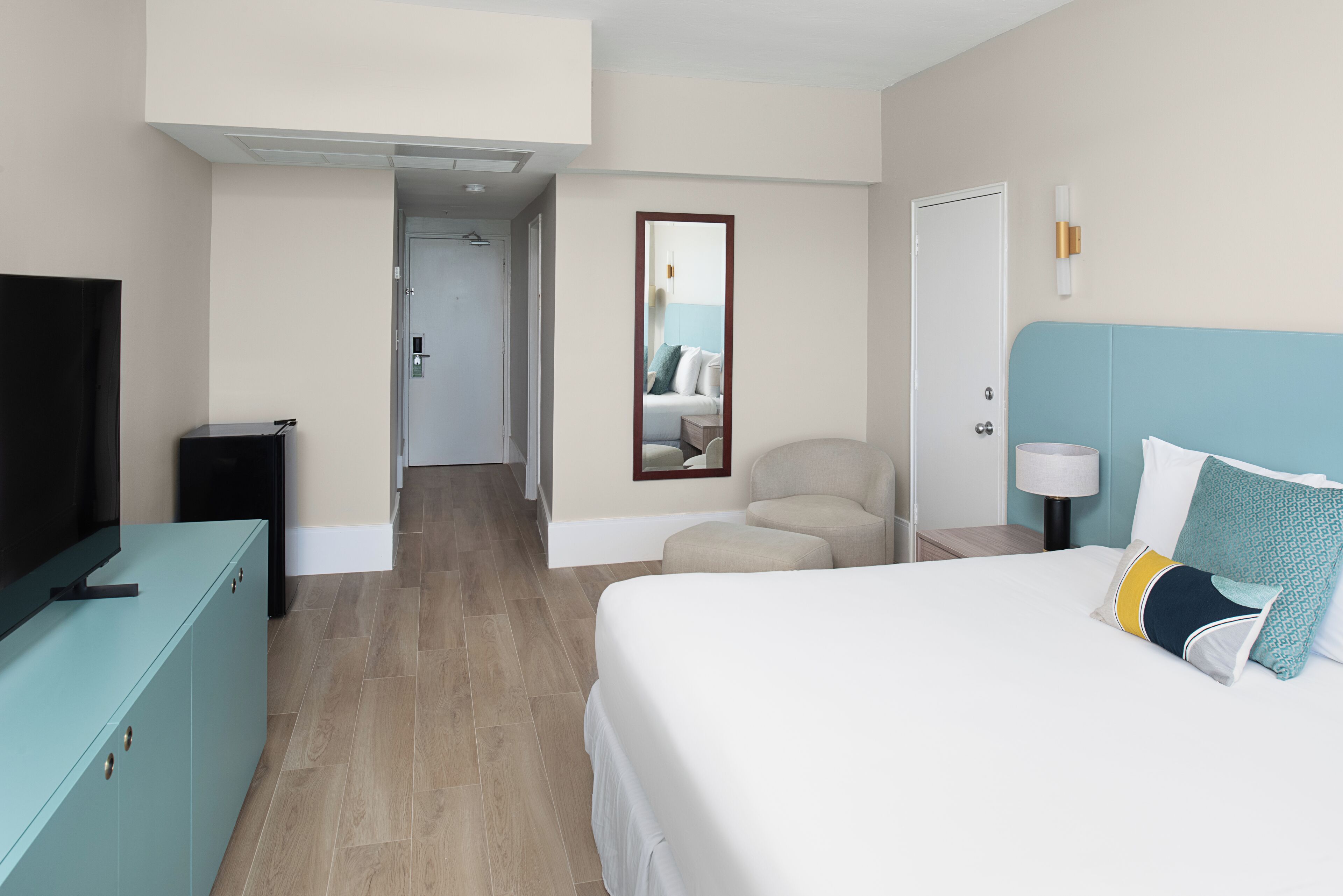A hotel room with a bed, a TV, a desk, and a mirror.
