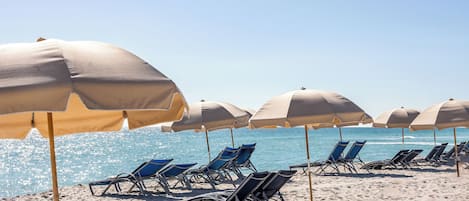 A beach with rows of sun umbrellas and lounge chairs facing the ocean.