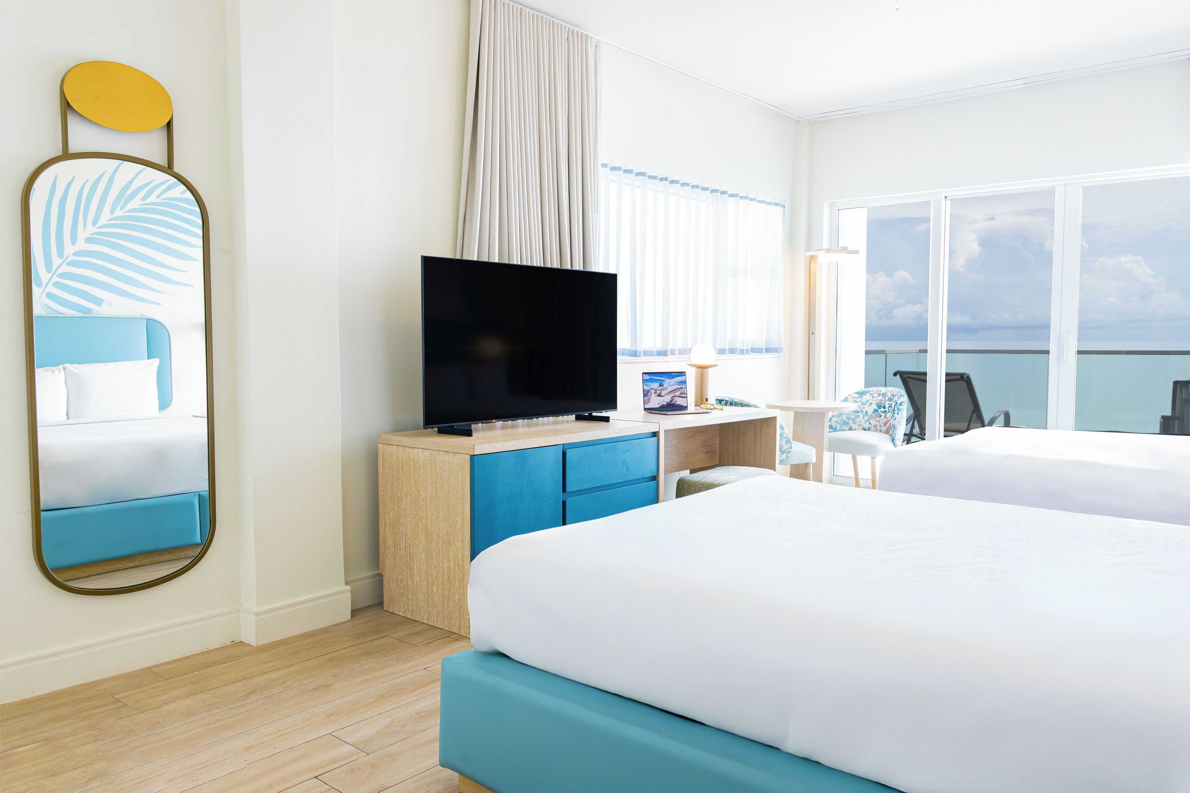A hotel room with a large bed, a TV, a desk with a chair, and a view of the sea.