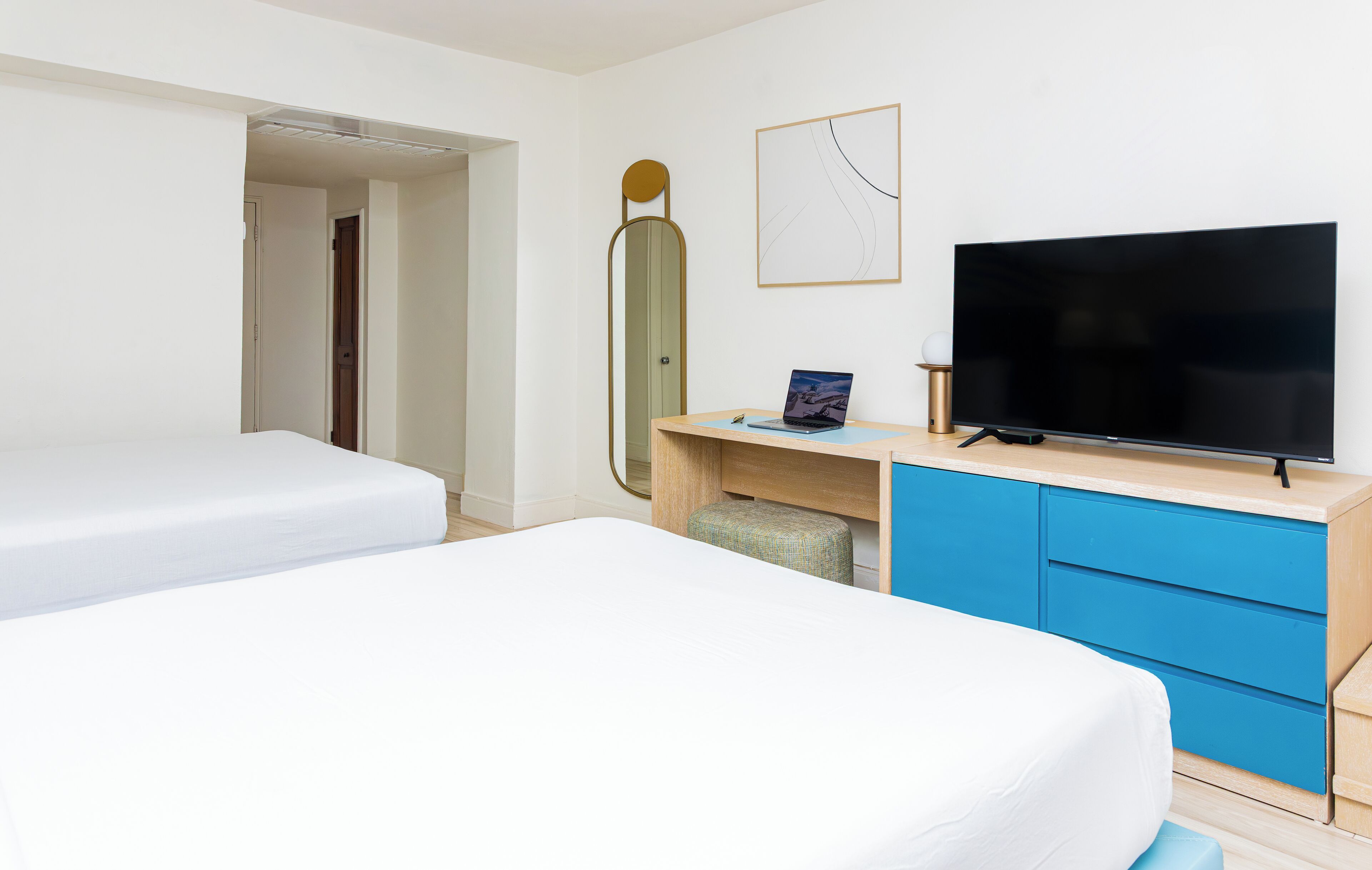 Une chambre d’hôtel avec deux lits, un bureau avec un ordinateur portable, une télévision et un grand miroir.