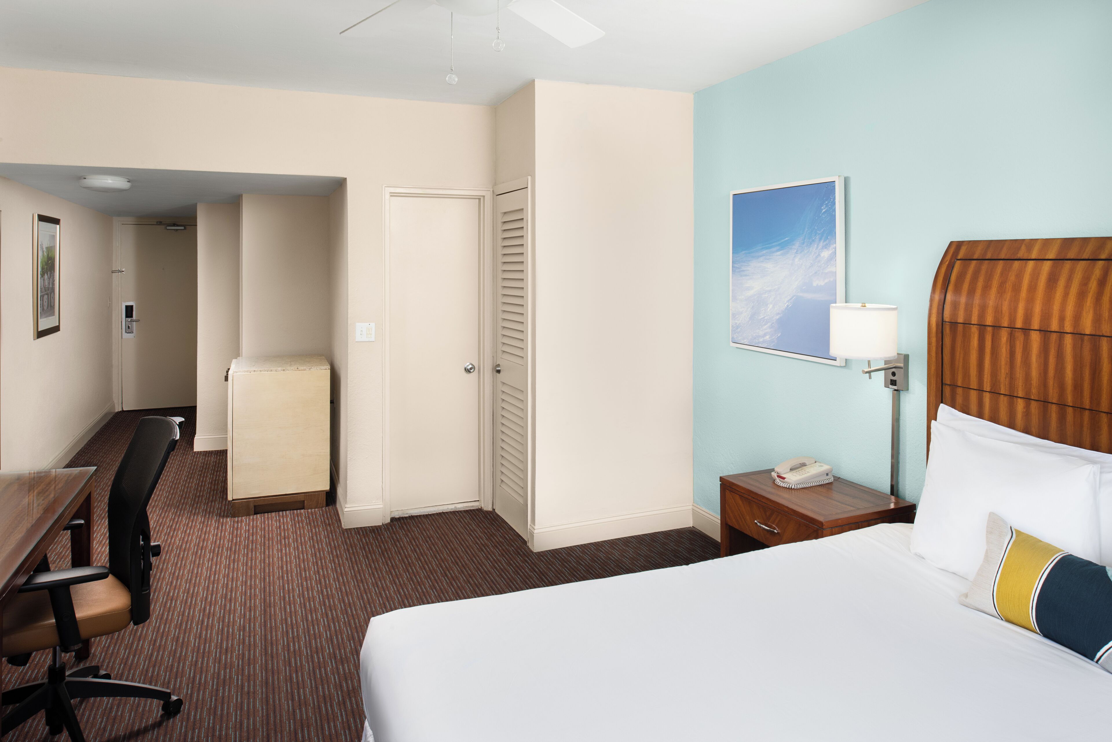 A hotel room with a bed, desk, chair, and a small kitchenette.