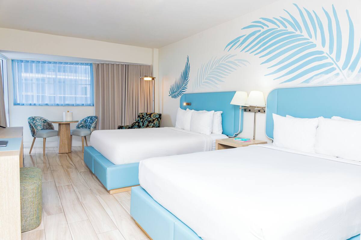 A hotel room with two beds, a desk, a chair, and a large window with curtains.