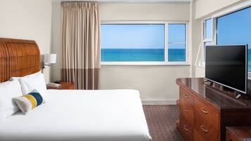 Habitación de hotel con una cama grande, televisión, cómoda de madera y ventana con vista al océano.