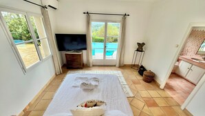 Un dormitorio con una cama grande, televisión, ventana con vista a una piscina y baño con piso de baldosas rosas.