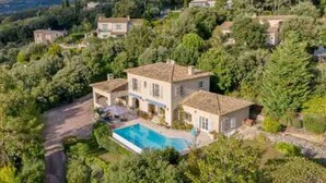 Una amplia villa con piscina rodeada de exuberante vegetación y colinas al fondo.