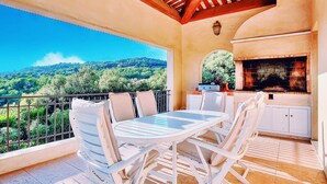 Un balcón con mesa y sillas, una chimenea de ladrillo y una vista panorámica de una colina boscosa.