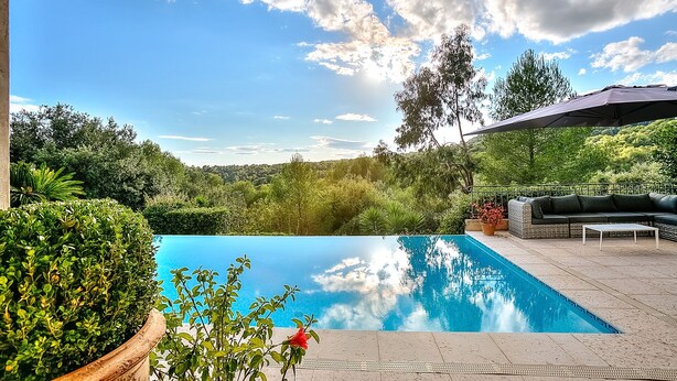 Una piscina con vistas a una ladera boscosa, un área de estar al aire libre cubierta y una pérgola.