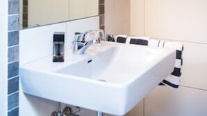 Ein modernes Badezimmer mit einem großen Spiegel, einem weißen Waschbecken und einer Topf-Orchidee.