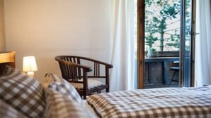 Ein Hotelzimmer mit Bett, Stuhl, Lampe und Blick auf einen Balkon mit Tisch und Stühlen.