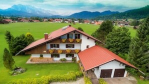 Ein zweistöckiges Haus mit rotem Dach, einem Balkon mit Pflanzen und einer Garage.