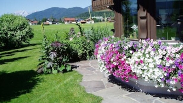 Ein Haus mit einem steinernen Weg, der zu einem Blumenbeet mit rosa und weißen Blumen führt.