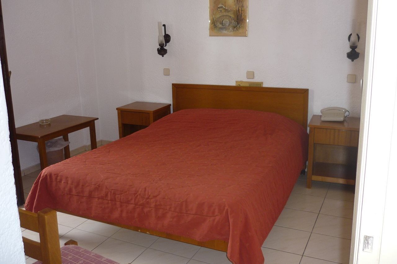 Une chambre à coucher avec un lit simple, une table de chevet, une commode et une lampe fixée au mur.