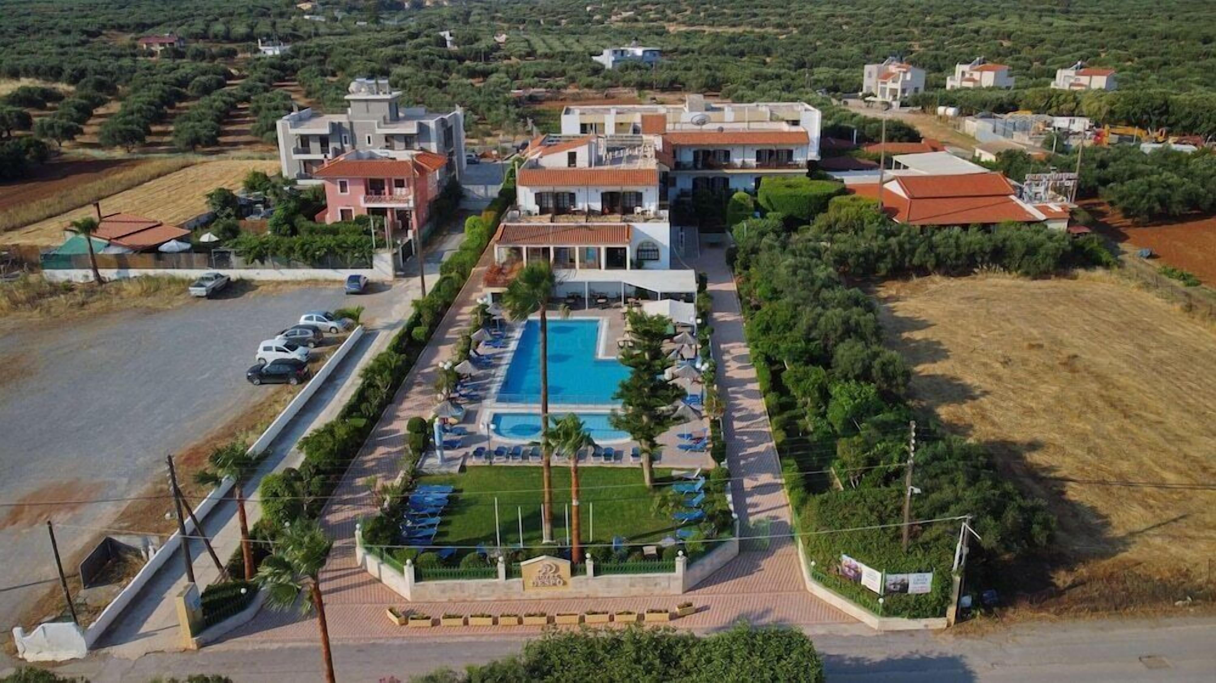 A large building with a swimming pool, surrounded by greenery and a parking area.