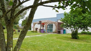 Un espace extérieur abrité doté d’une structure en bois, d’un chemin et d’un bâtiment en arrière-plan.
