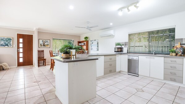 A modern kitchen with a central island, white cabinetry, and a large window with blinds. - Starview Agnes Water (Agnes Water)