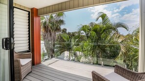 A balcony with wicker furniture, a glass railing, and a view of palm trees. - Starview Agnes Water (Agnes Water)