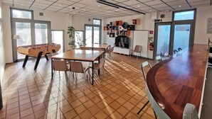 A spacious room with a foosball table, a long dining table, and a TV. - Auberge de Jeunesse HI Boulogne-sur-Mer (Boulogne-sur-Mer)