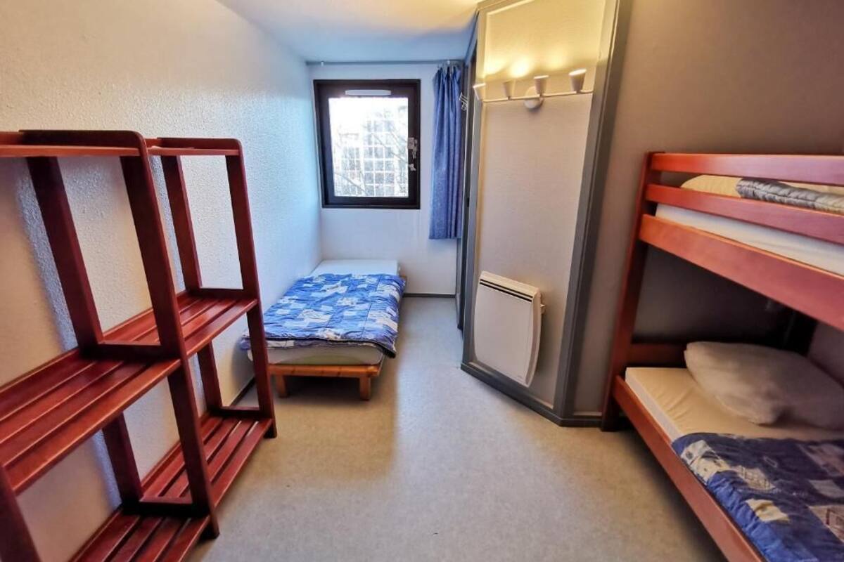 Et lille værelse med to køjesenge, et lille vindue med gardiner, en radiator og en hylde.