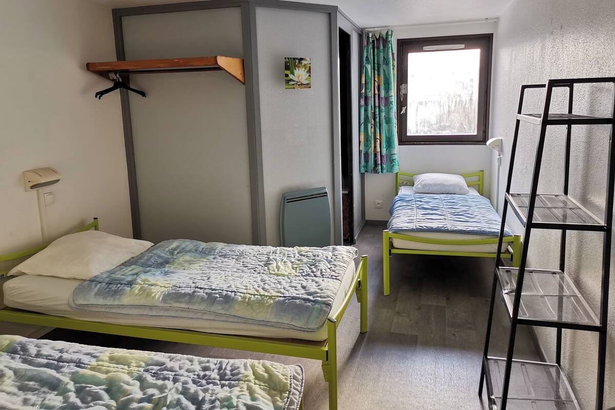 Et sovesalsværelse med to køjesenge, et lille skrivebord, en stol, en radiator og et vindue med gardiner.