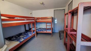 Un dormitorio con literas, un calentador pequeño, una puerta y una escalera.