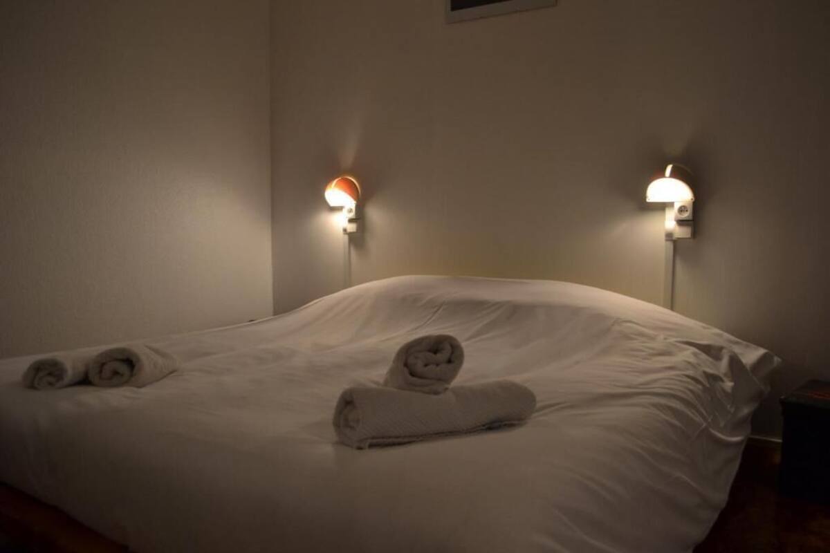 Et hotelværelse med en pænt redt seng, to vægmonterede lamper og foldede håndklæder på sengen.