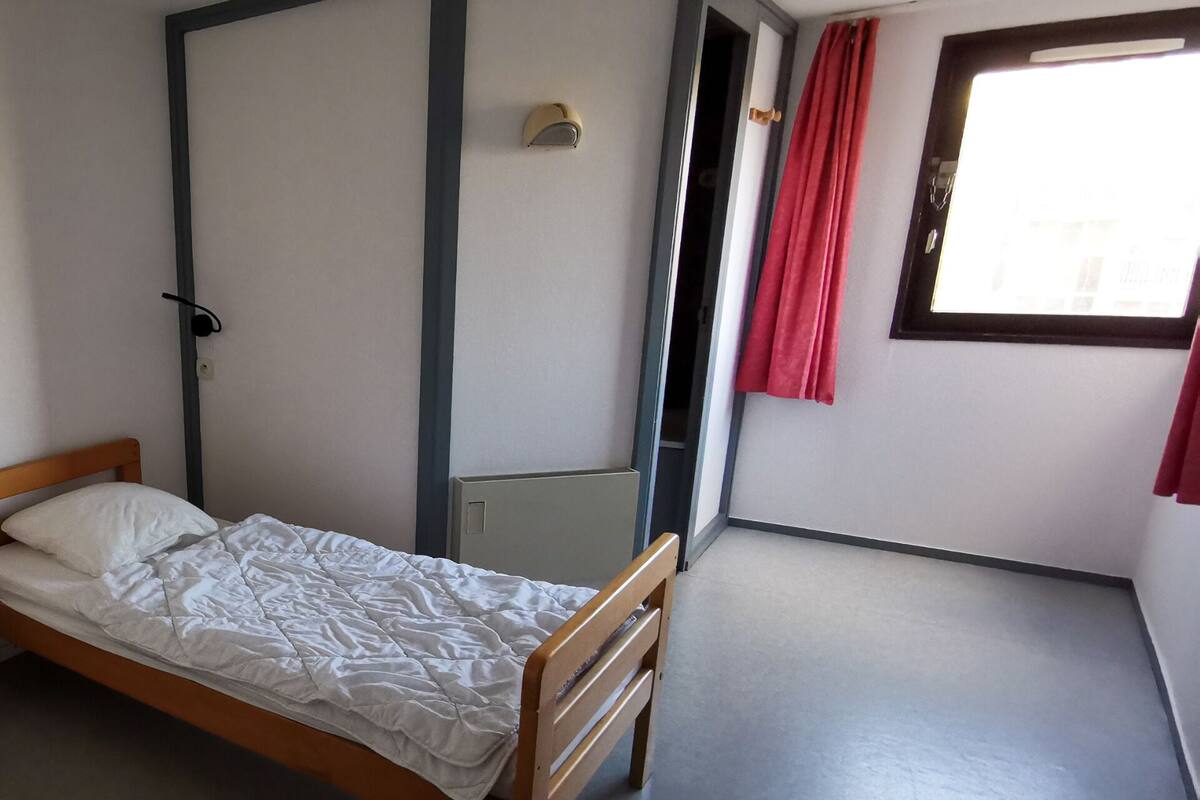 En seng med træramme og hvide sengetøj i et rum med grå gulv og hvide vægge.