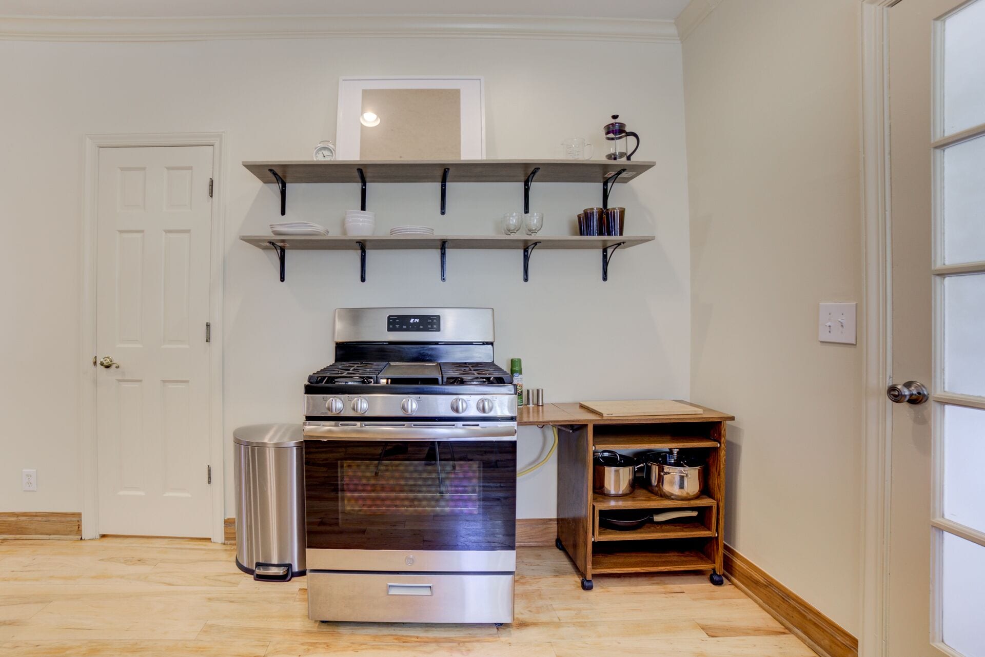 A kitchen with a stove, oven, and shelves above holding dishes and glasses.