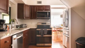 A modern kitchen with dark wooden cabinets, stainless steel appliances, and a wooden floor.