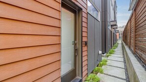 Un sendero estrecho bordeado por revestimiento de madera y una fachada de edificio moderna con puerta de vidrio.
