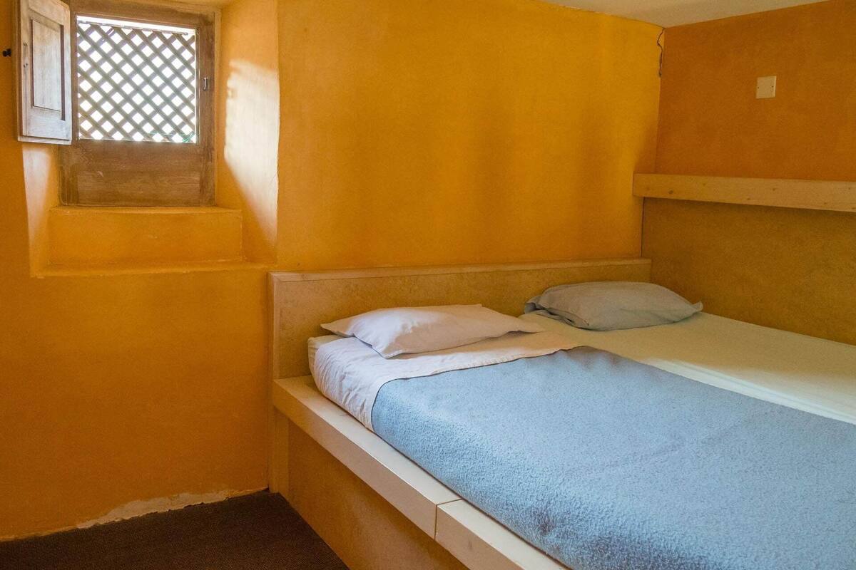 Une petite chambre avec un lit simple, une fenêtre et un lit superposé.