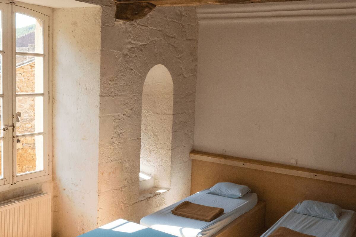 Une chambre avec deux lits simples, une fenêtre et un mur en pierre.