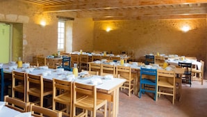 Un comedor rústico con mesas y sillas de madera, paredes de piedra y vigas de madera a la vista en el techo.