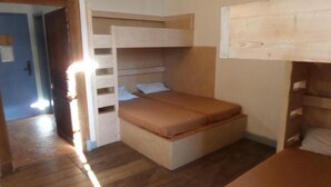 Una habitación pequeña con una cama nido, una cama individual y piso de madera.