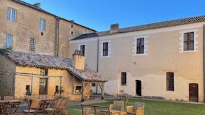 Un patio con mobiliario exterior y un edificio de paredes de piedra y techos de tejas.