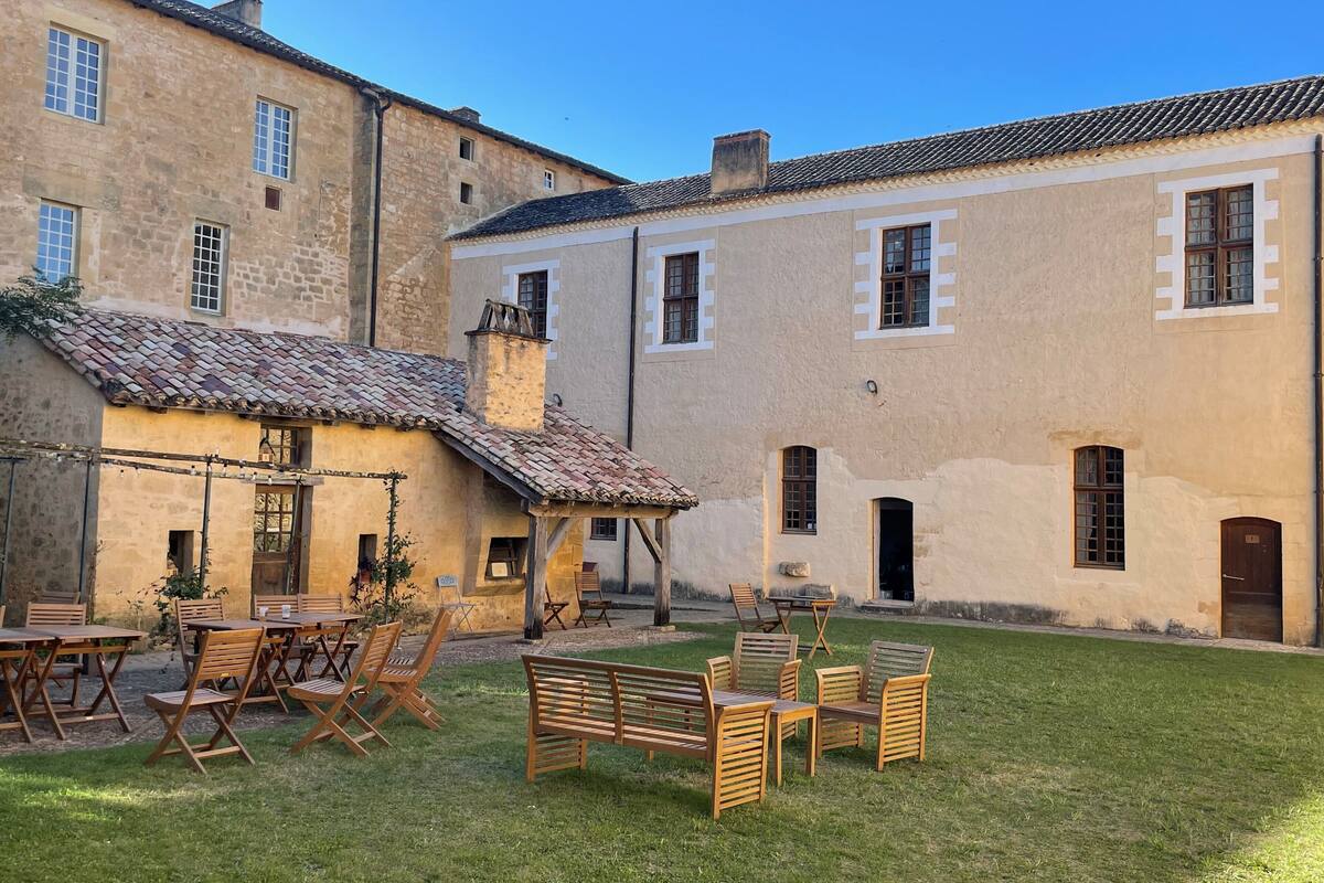 Une cour dotée d’un espace extérieur aménagé avec des sièges, ainsi qu’un bâtiment aux murs en pierre et aux toits couverts de tuiles.