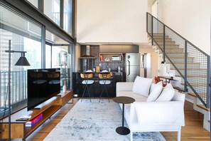A modern living room with a large flat-screen TV, a white sofa, a coffee table, and a kitchen in the background. - Huma Itaim  (São Paulo)