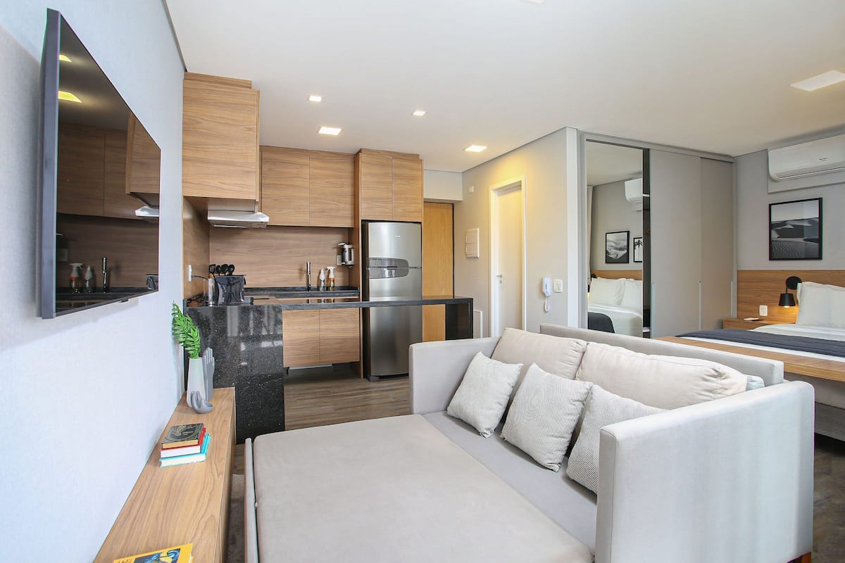 Una habitación de hotel moderna con kitchenette, un sofá, una mesita de noche y un espejo.