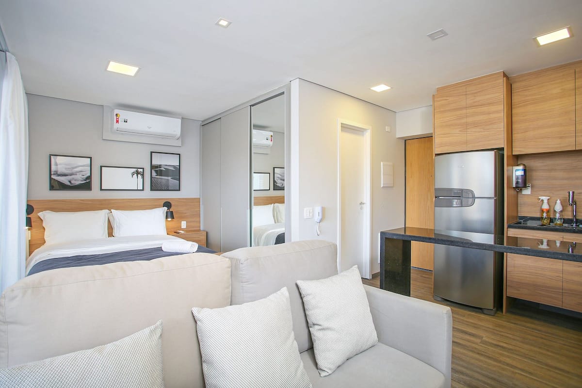 Una habitación de hotel moderna con cama, sofá, kitchenette y aire acondicionado integrado.