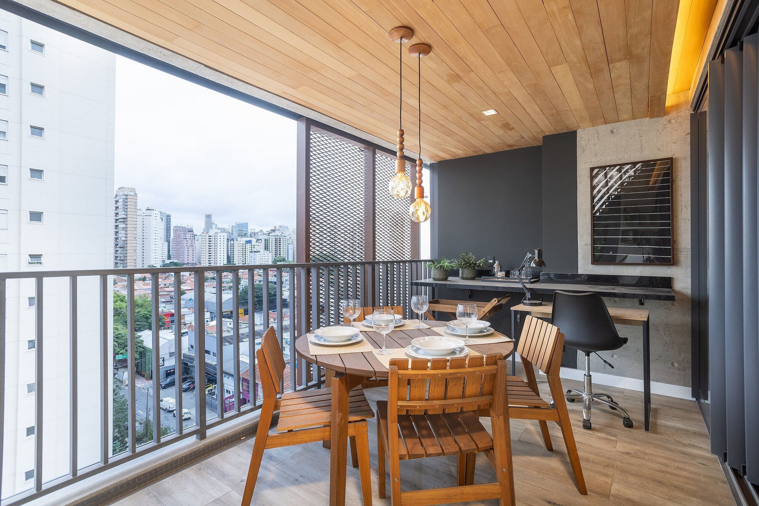 A balcony with a dining table set for four, a kitchen area, and a city view.