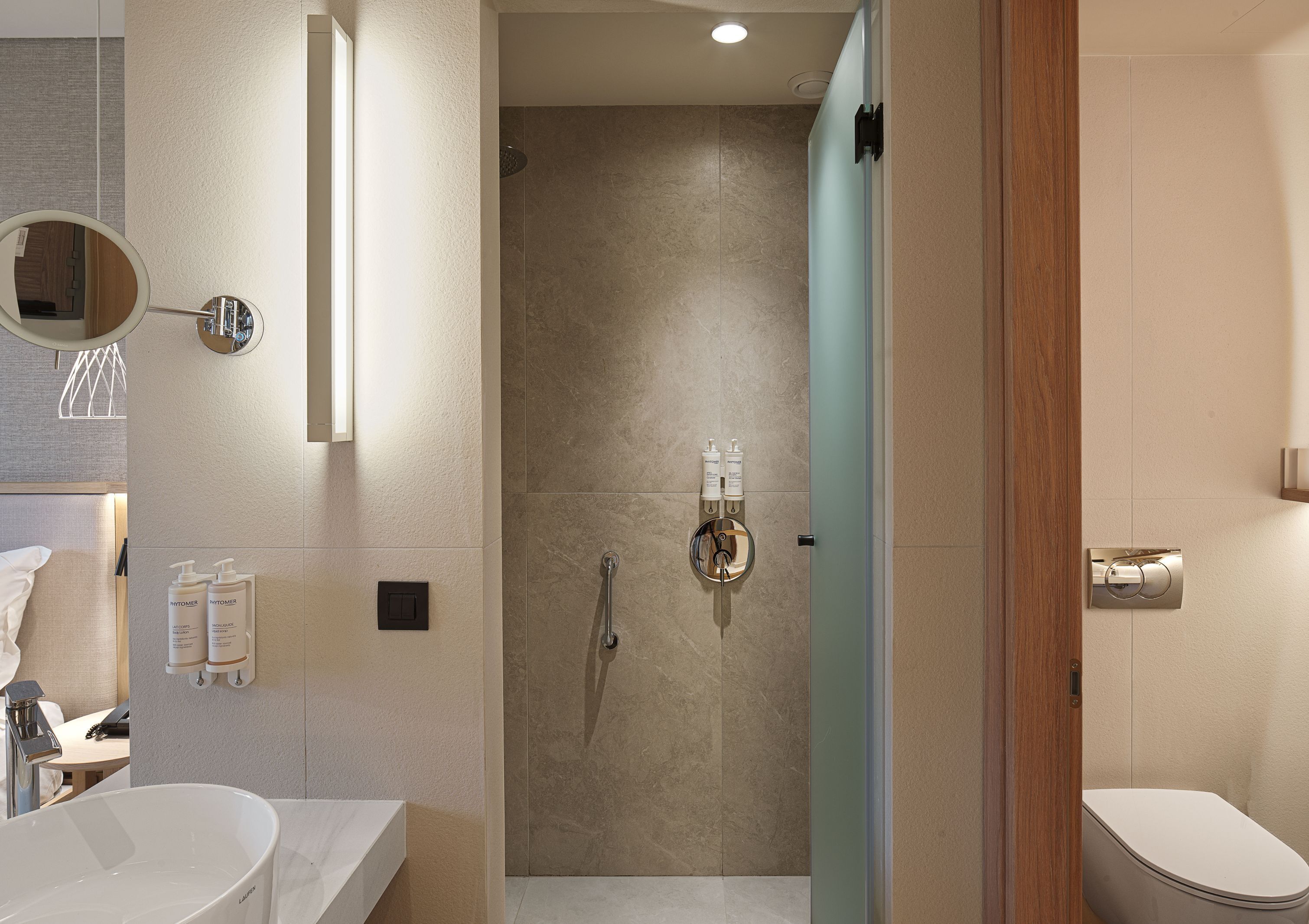 A modern bathroom with a large mirror, a sink, a shower with a glass door, and toiletries on the wall.